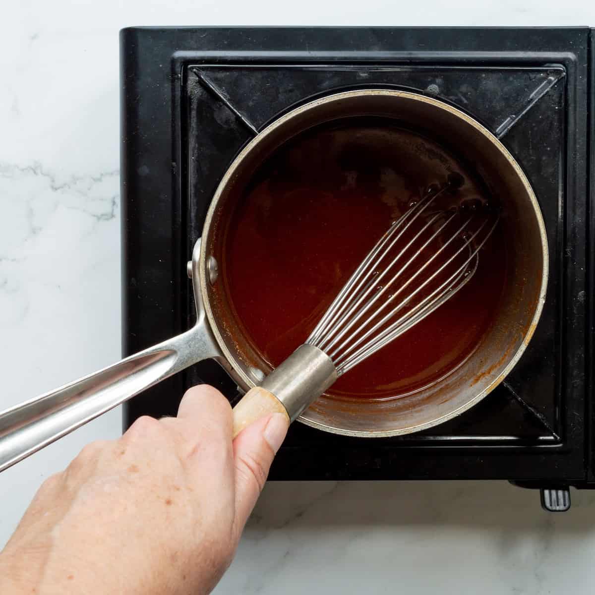 Heating the ingredients for Western NC BBQ Sauce recipe in a small saucepan and stirring with a whisk.