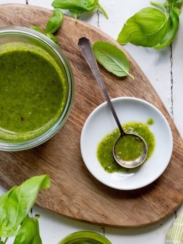Glass Weck jar of basil balsamic vinaigrette on an oval wooden cutting board and a small white dish with a spoon and some vinaigrette.