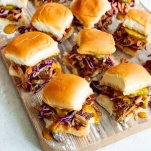 Wooden board topped with BBQ Pulled Pork Sliders with a yellow cloth in the background.