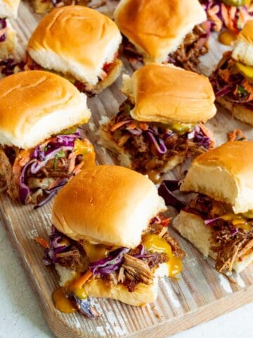 Wooden board topped with BBQ Pulled Pork Sliders with a yellow cloth in the background.