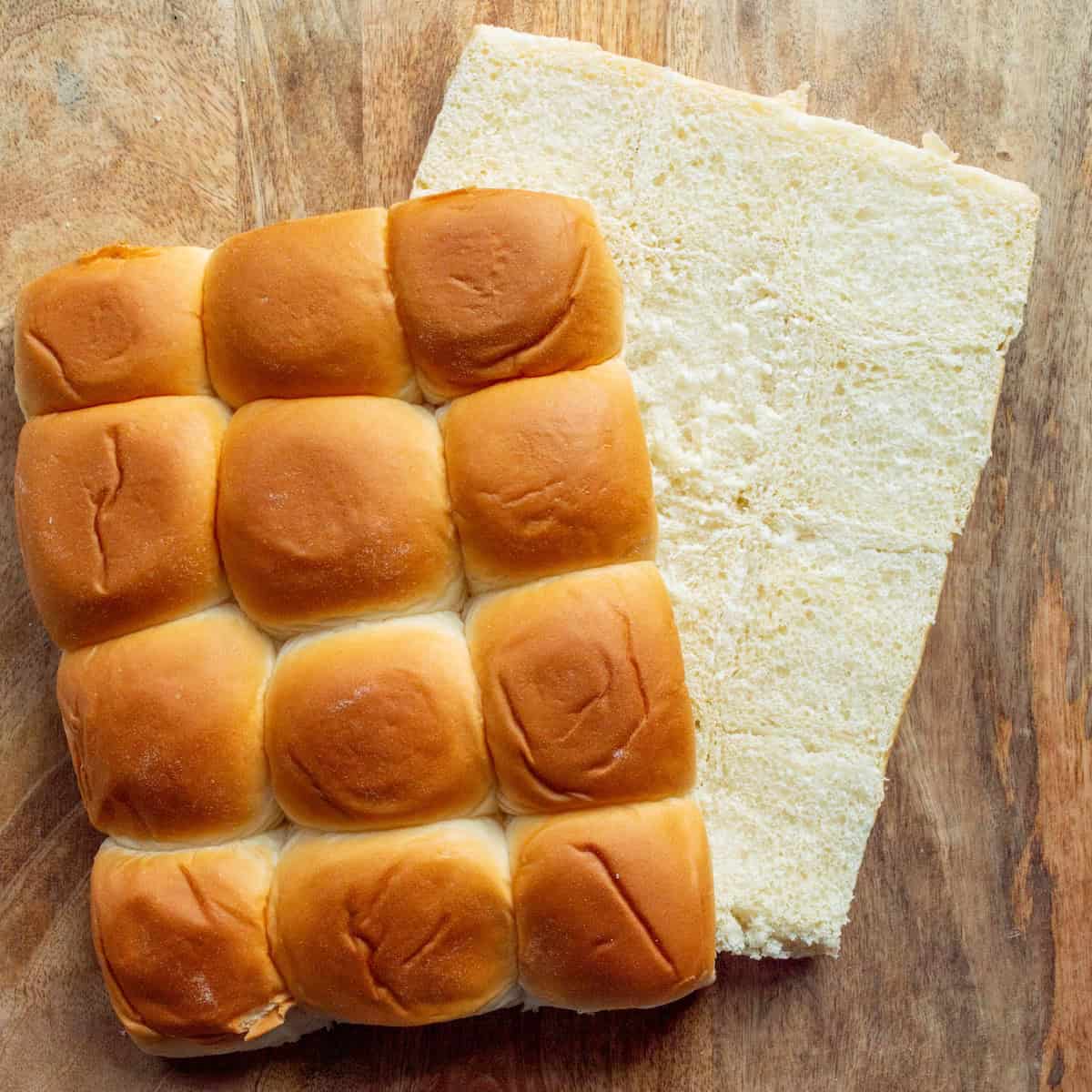 A package of Hawaiian rolls out of their package and split horizontally on a wooden board.