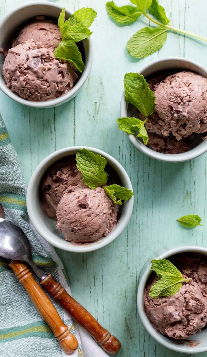 Four bowls of chocolate mint chocolate chip ice cream on a green surface with wooden handled spoons and a green striped cloth.