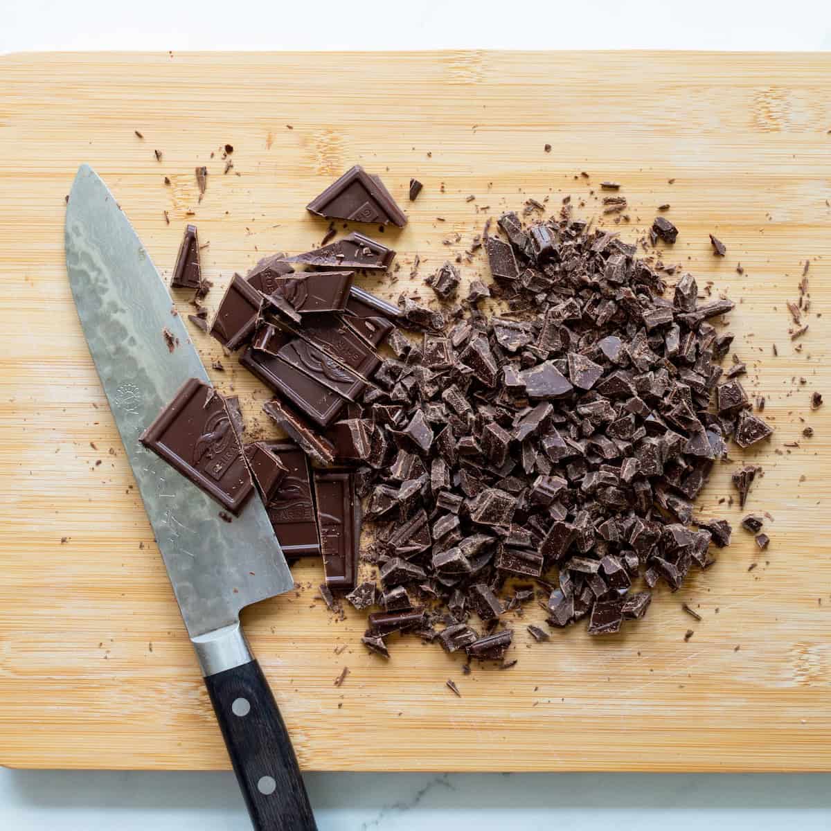 Chopped Ghirardelli chocolate bars on a wooden cutting board with a chef's knife off to the side.