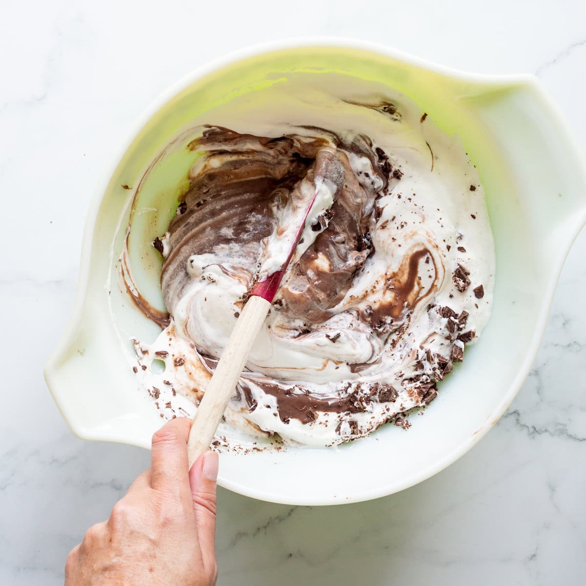 Folding together whipped cream, chocolate pudding, and chopped chocolate in a vintage Pyrex bowl.