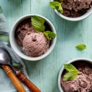 Bowls of chocolate mint chocolate chip ice cream on a green surface with wooden handled spoons and a green striped cloth.