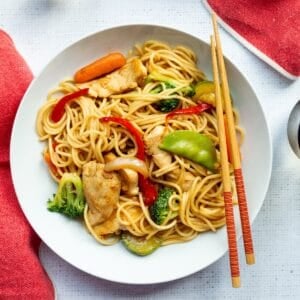 White bowl of PF Chang's Chicken Lo Mein with a pair of chopsticks and a red linen napkin.