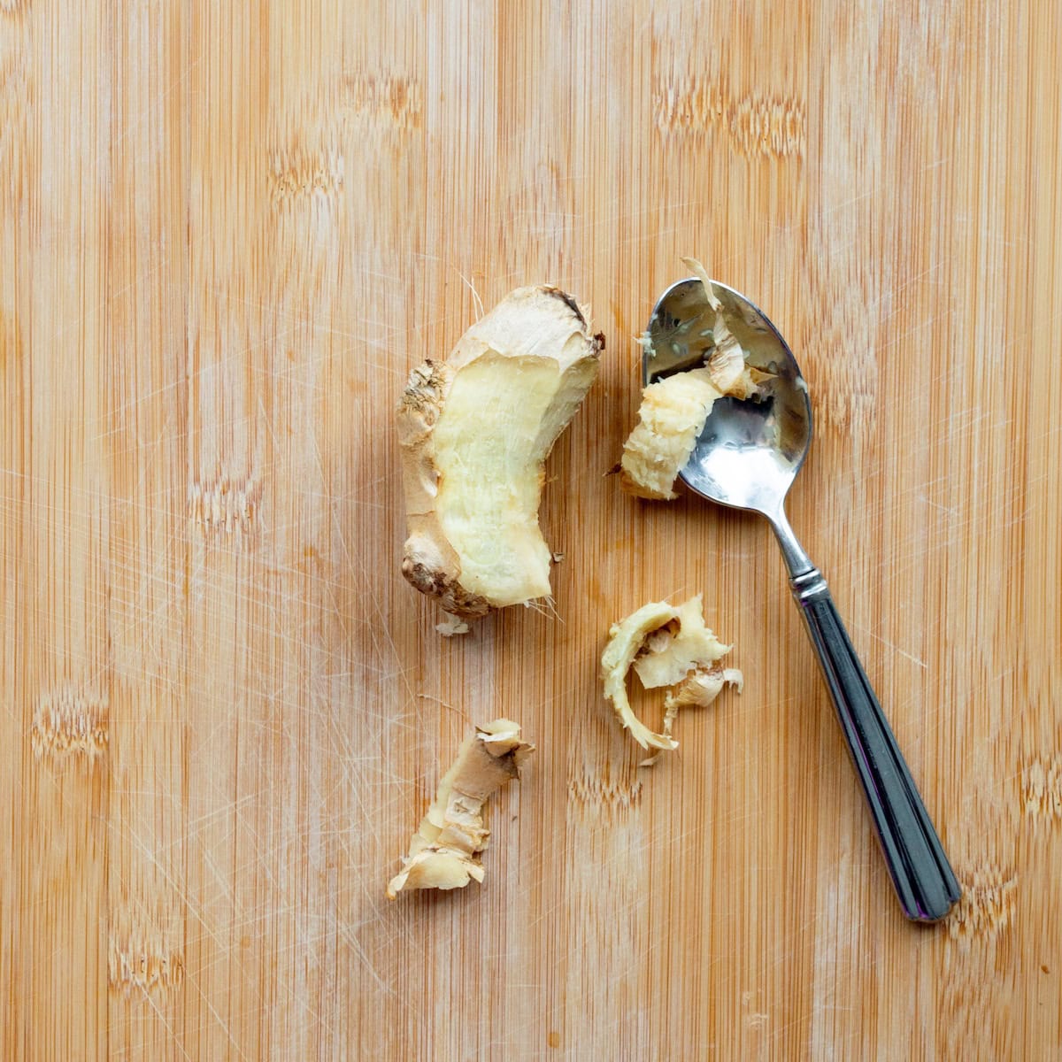 Peeling ginger with a spoon on a wooden cutting board.