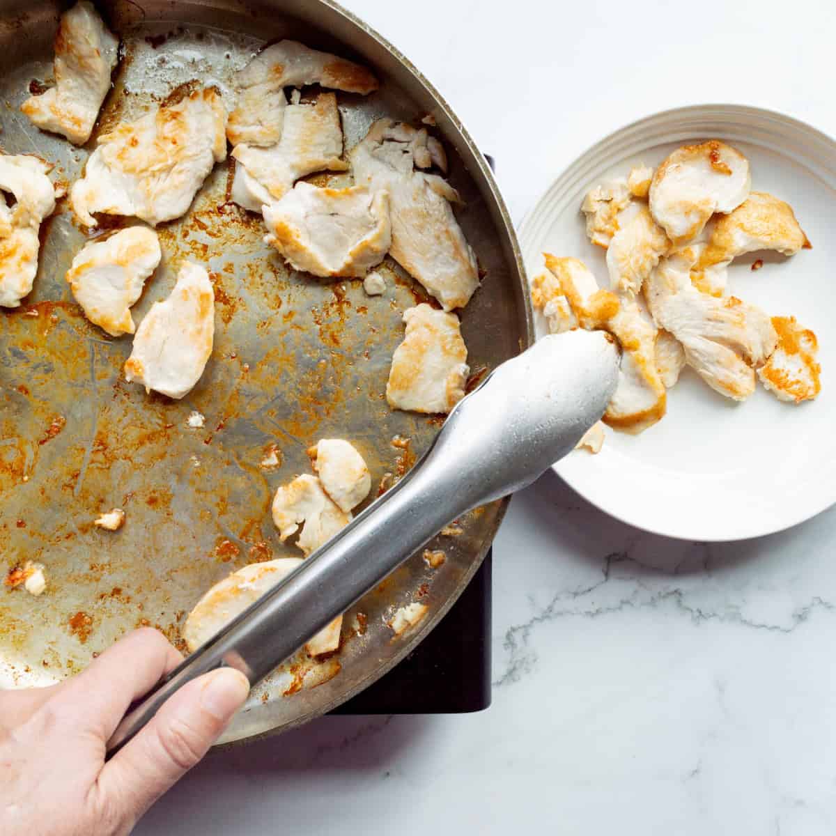 Browning pieces of chicken in a skillet and removing to a bowl with metal tongs.