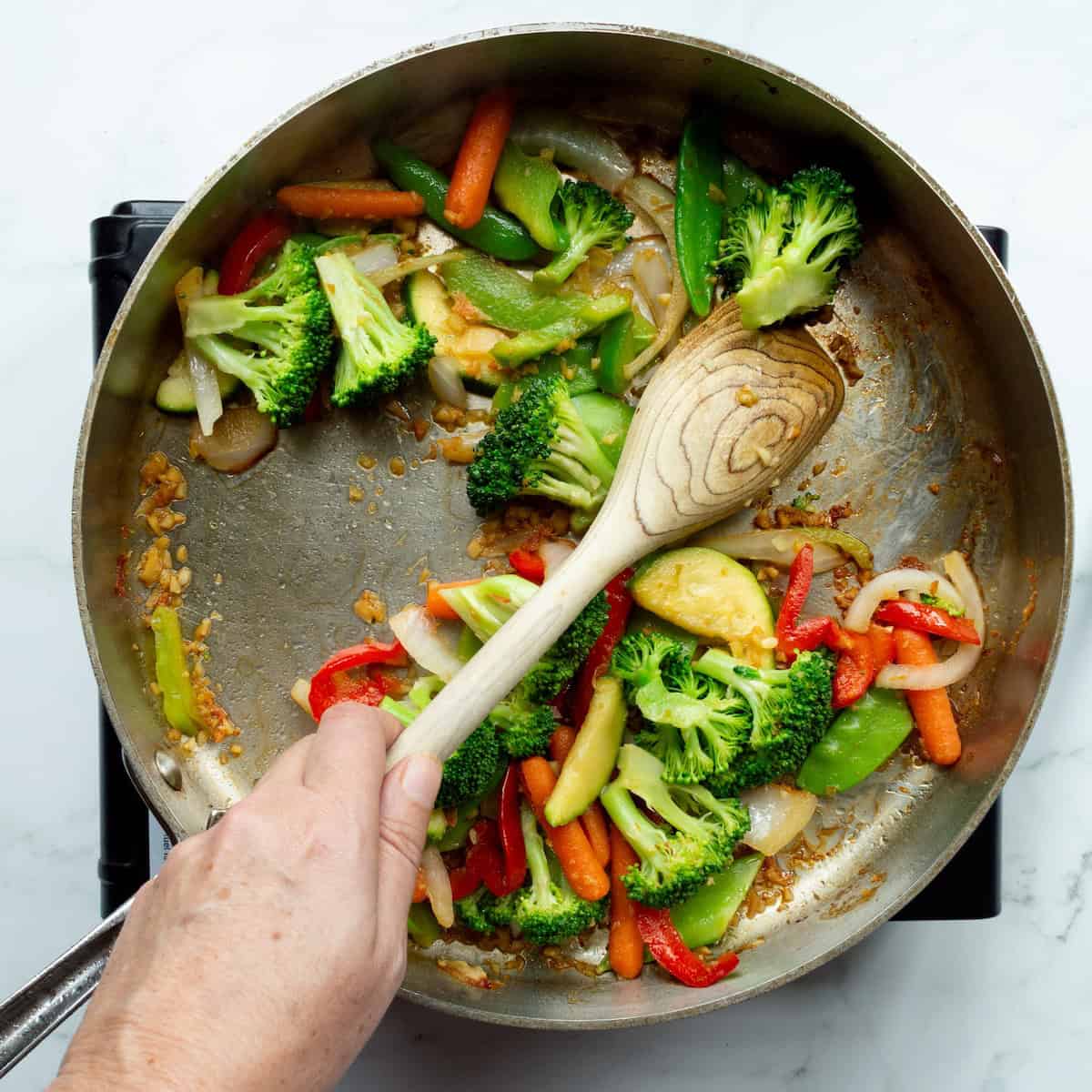 Sautéing stir-fry vegetables in a large skillet with a wooden spoon.