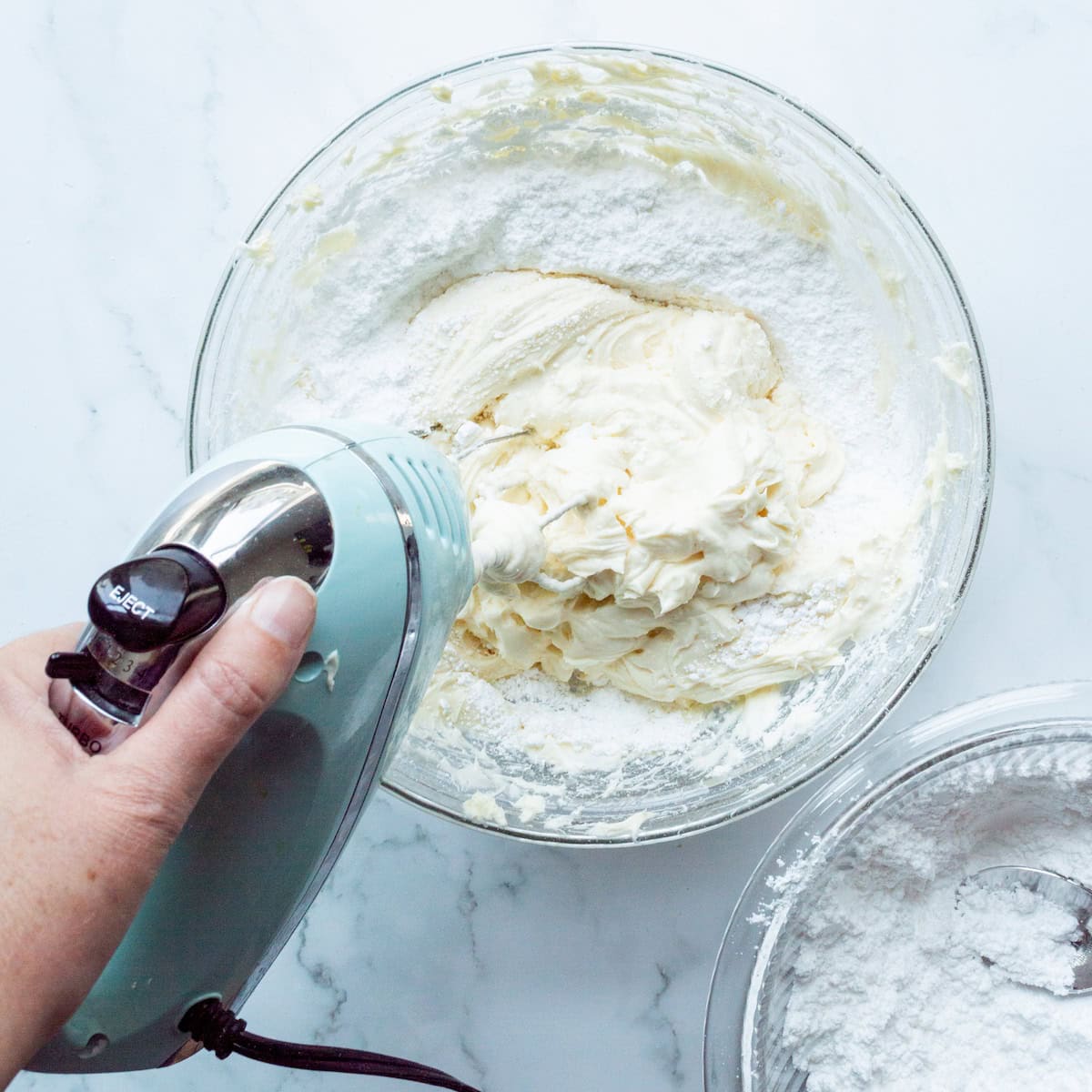 Beating powdered sugar into cream cheese and butter for cream cheese frosting in a glass bowl.