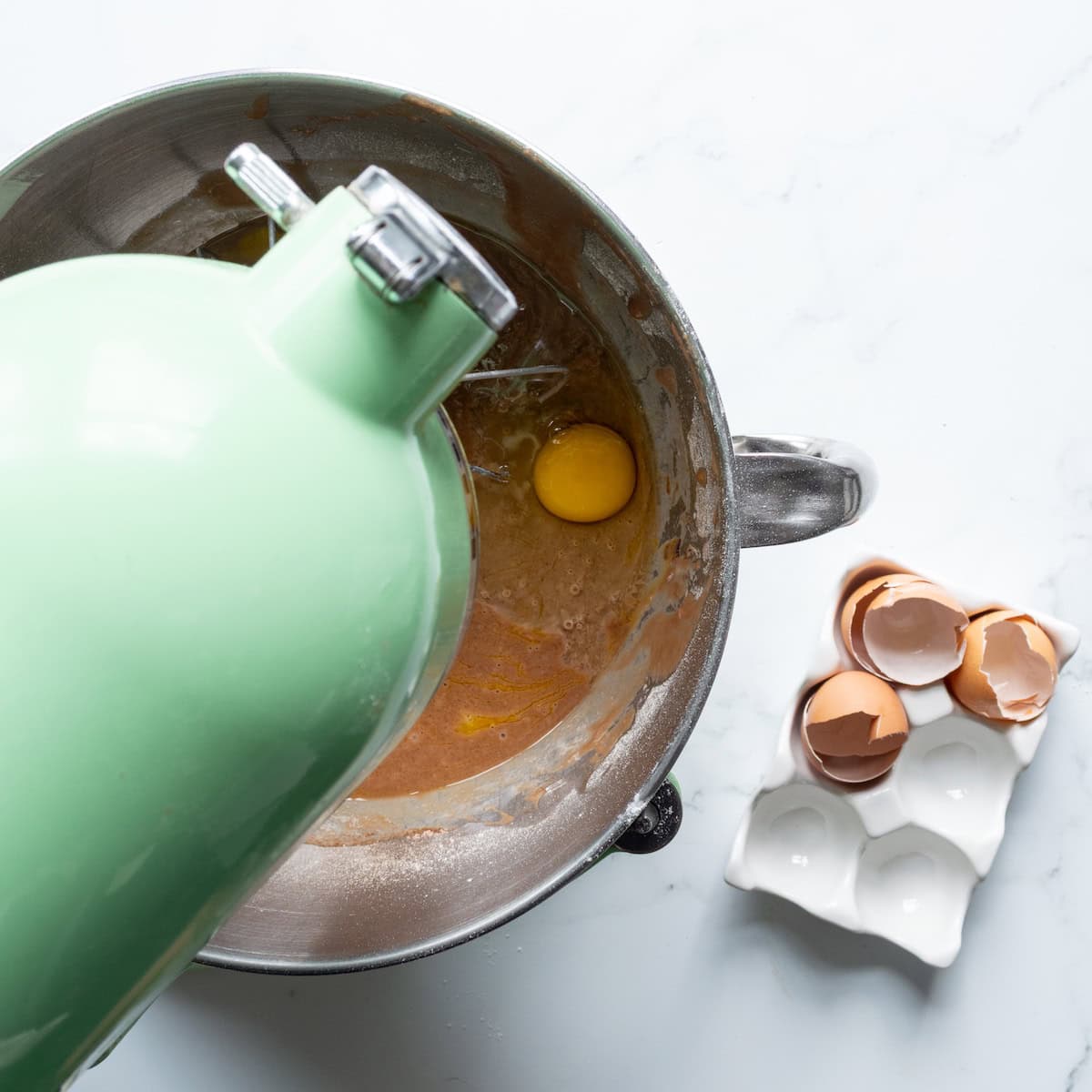 An egg cracked into a bowl of red velvet cake batter in a green mixer.