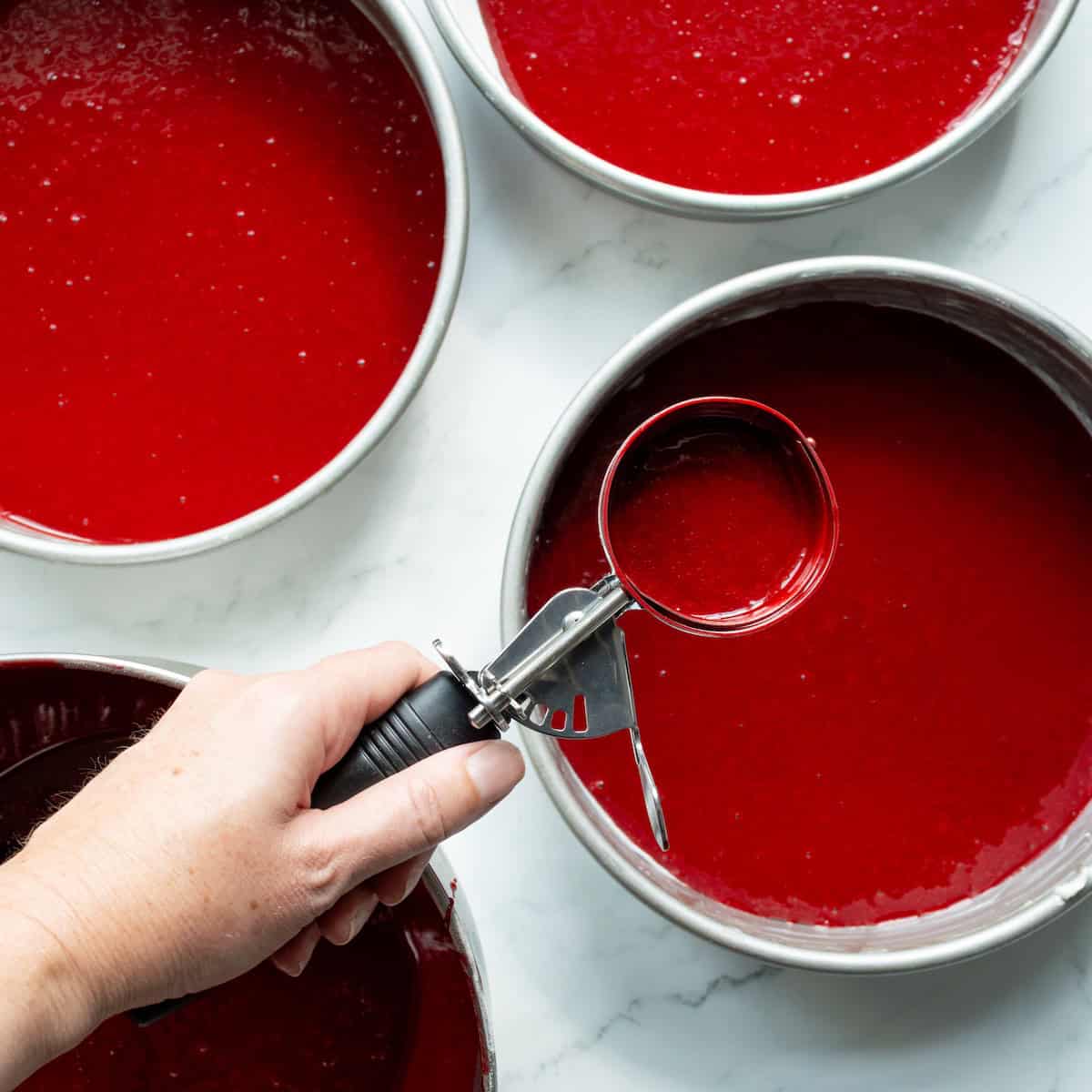 Dividing red velvet cake batter between cake pans.
