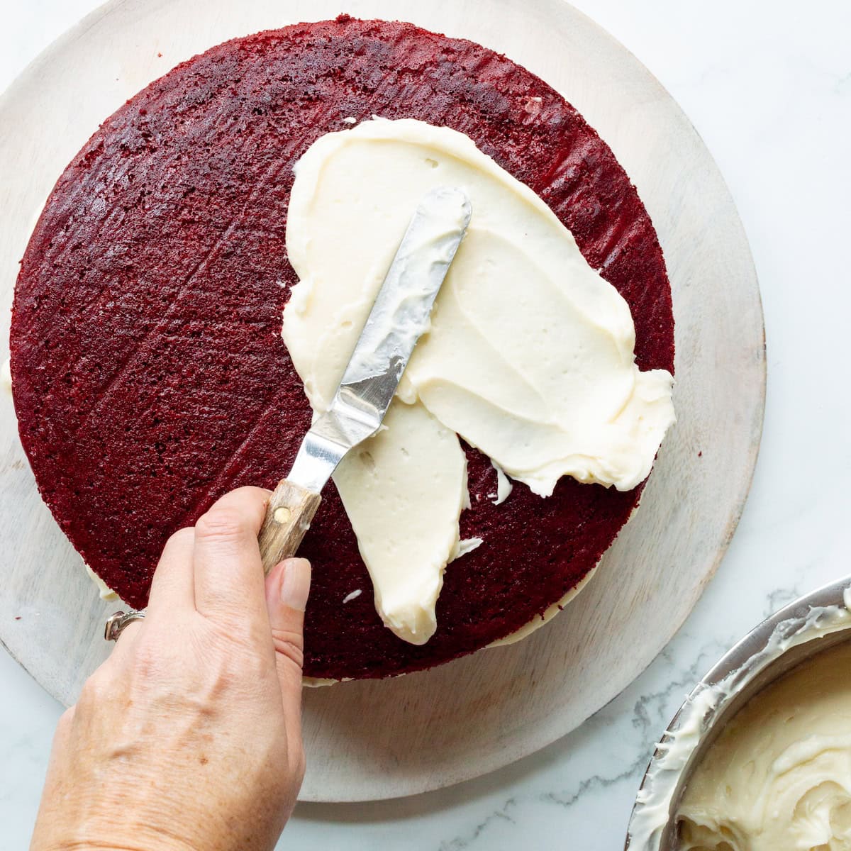 Spreading cream cheese frosting onto red velvet cake.