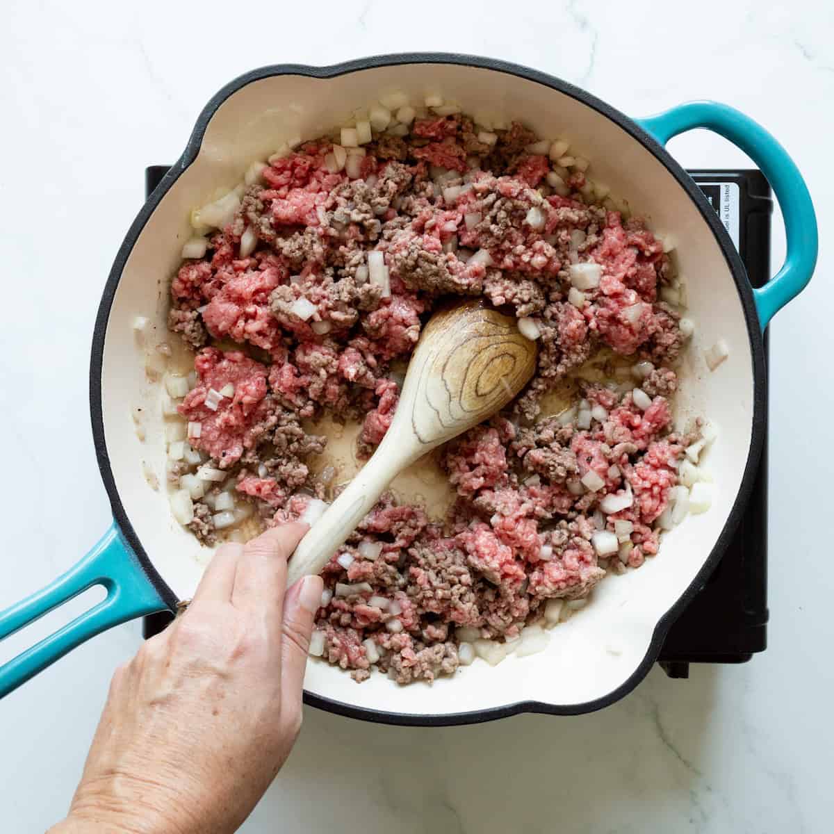Browning ground beef and onion in a teal-handled skillet with a wooden spoon.