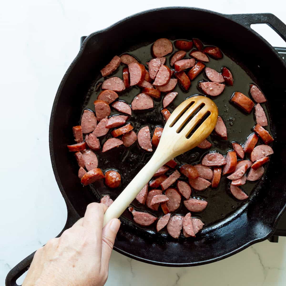 Browning pieces of smoked sausage in a cast-iron skillet.