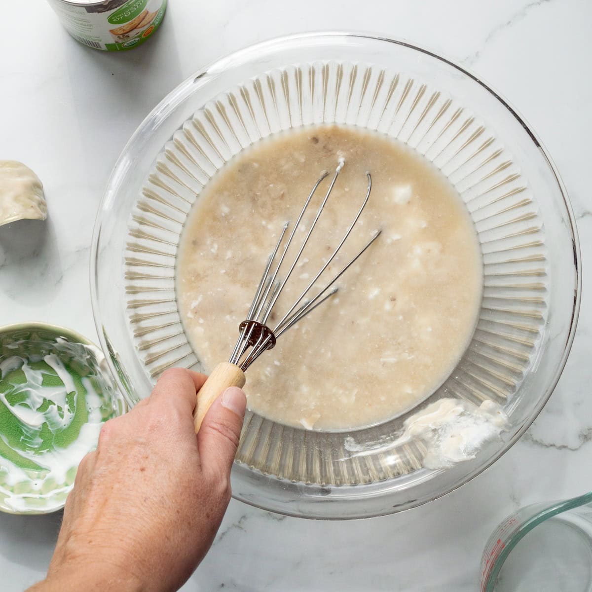 Whisking together sour cream, cream of mushroom soup, and chicken broth in a glass bowl.