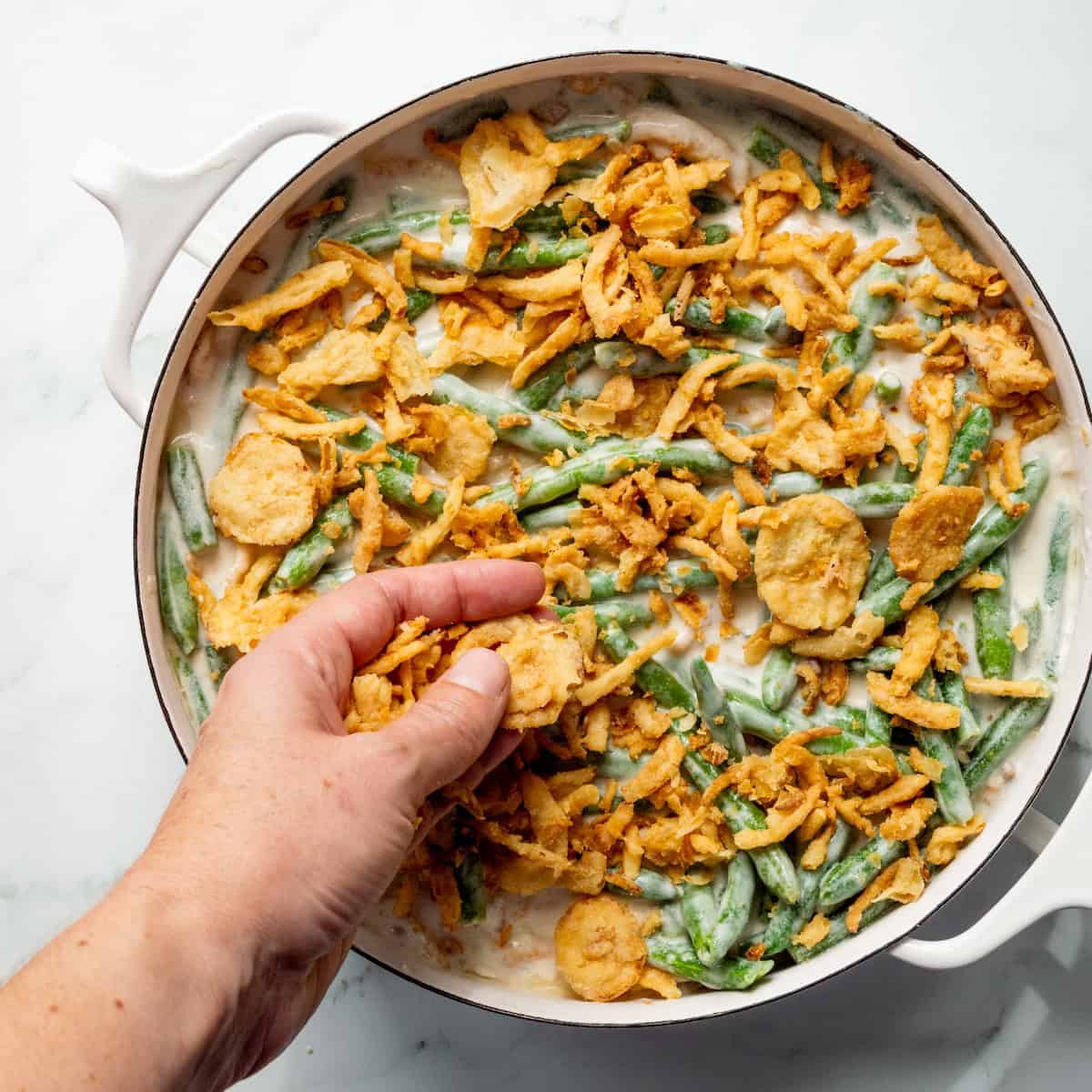 Topping green bean casserole in a white round dish with French's fried onions.