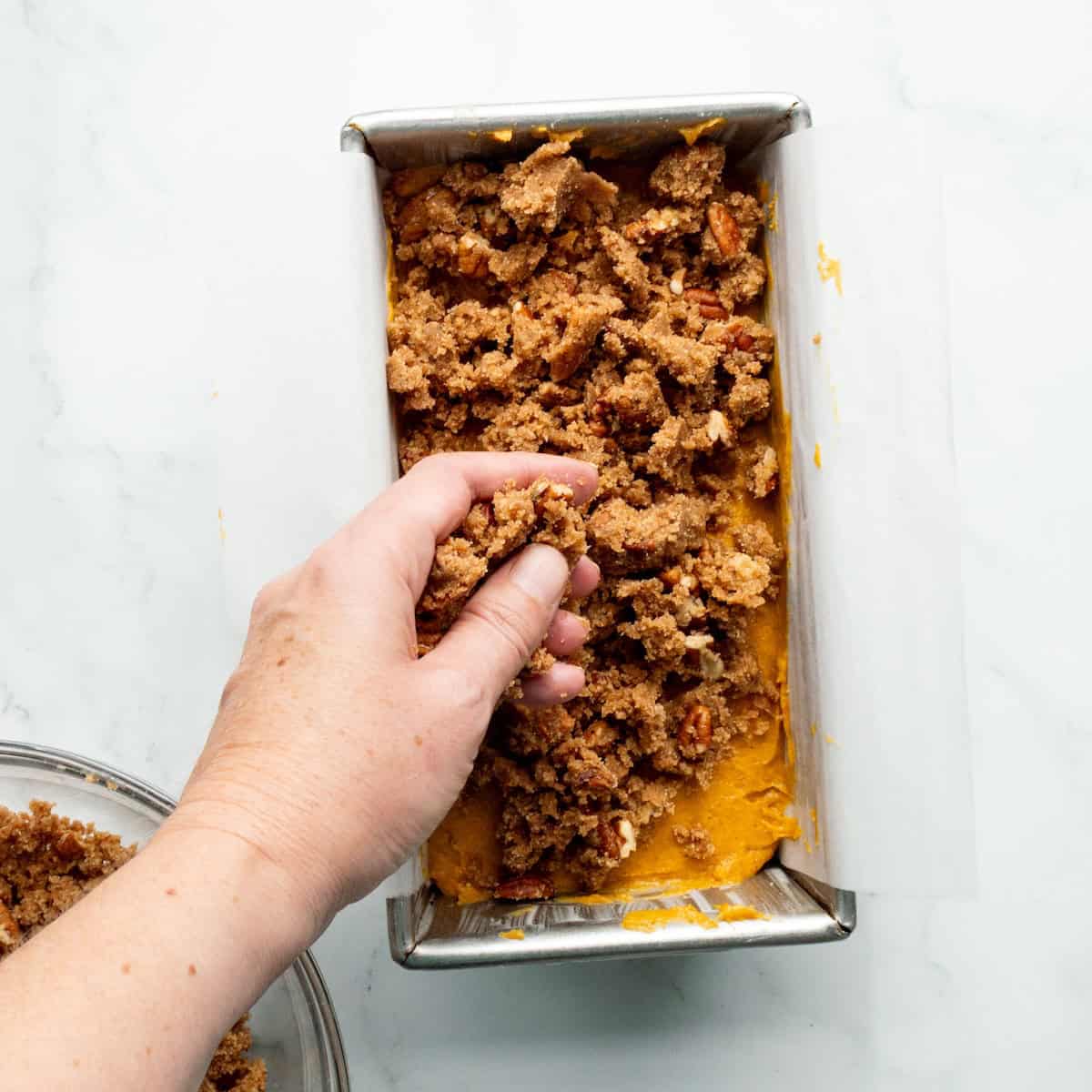 Adding streusel to the top of pumpkin bread batter in a loaf pan.