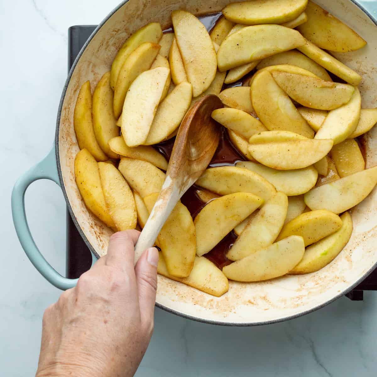 Cooking apples in a blue-handled large skillet.