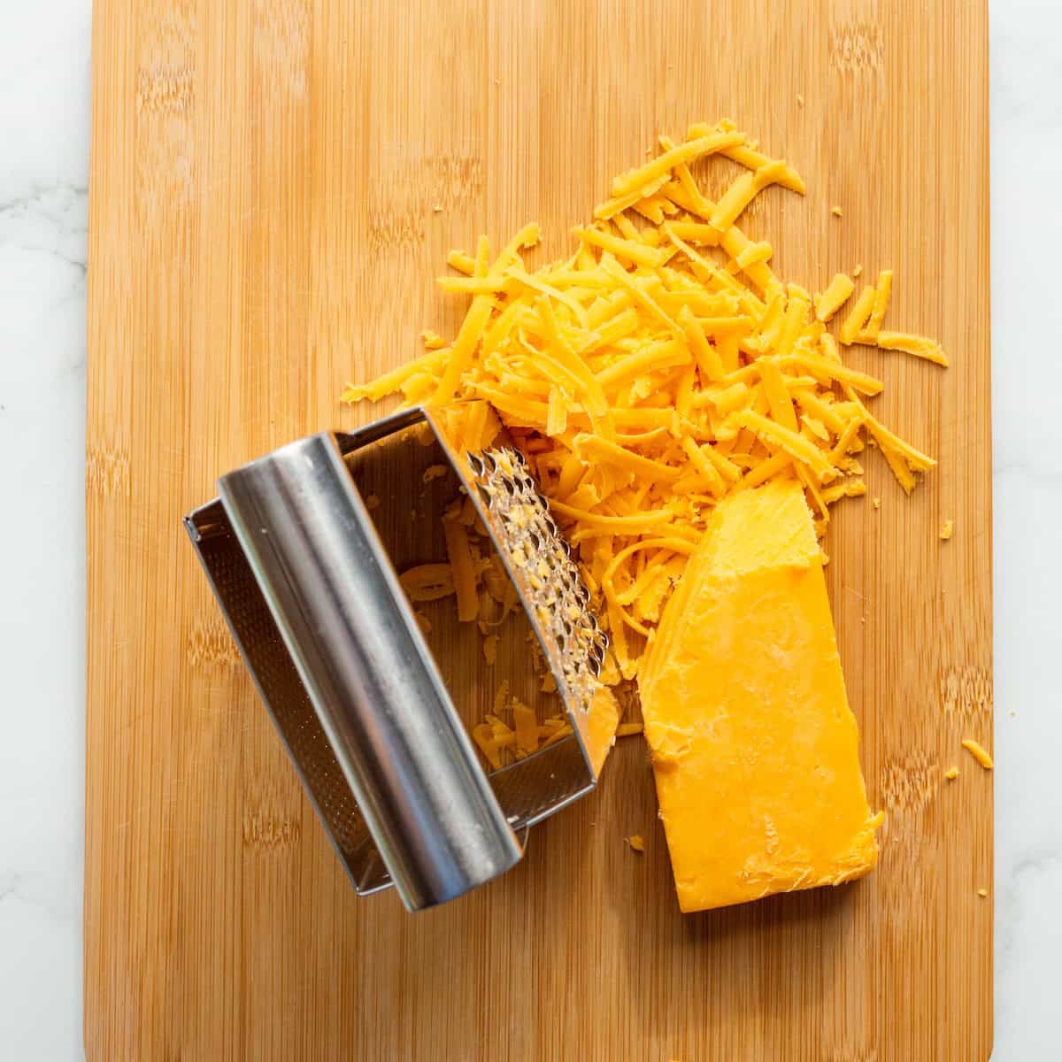 Grated sharp Cheddar cheese with a box grater on a wooden board.
