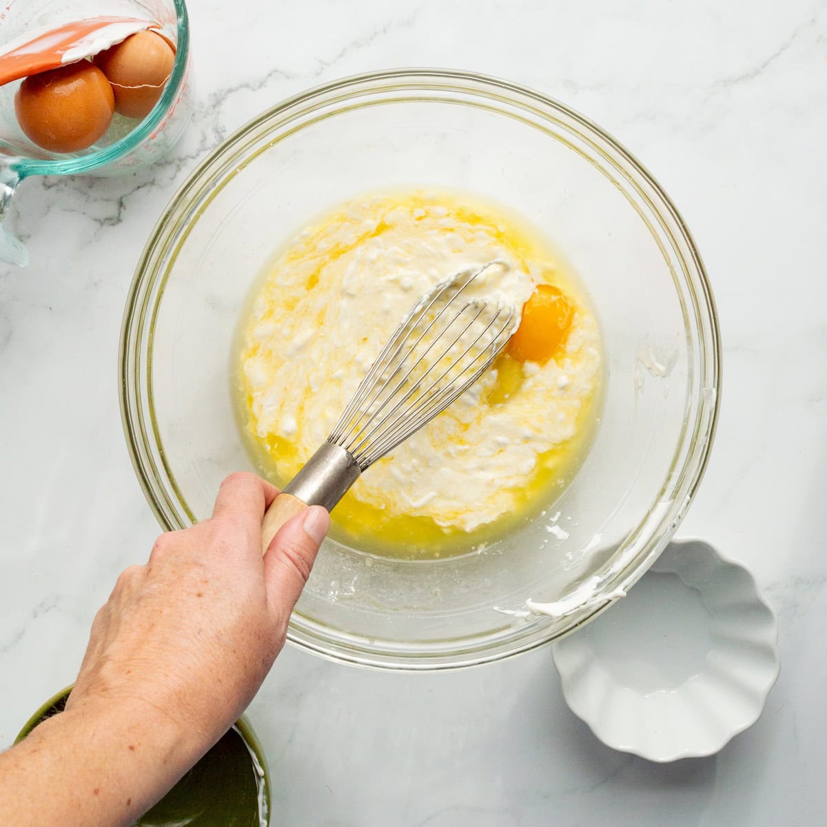 Whisking together butter, sour cream, and an egg in a large glass bowl.
