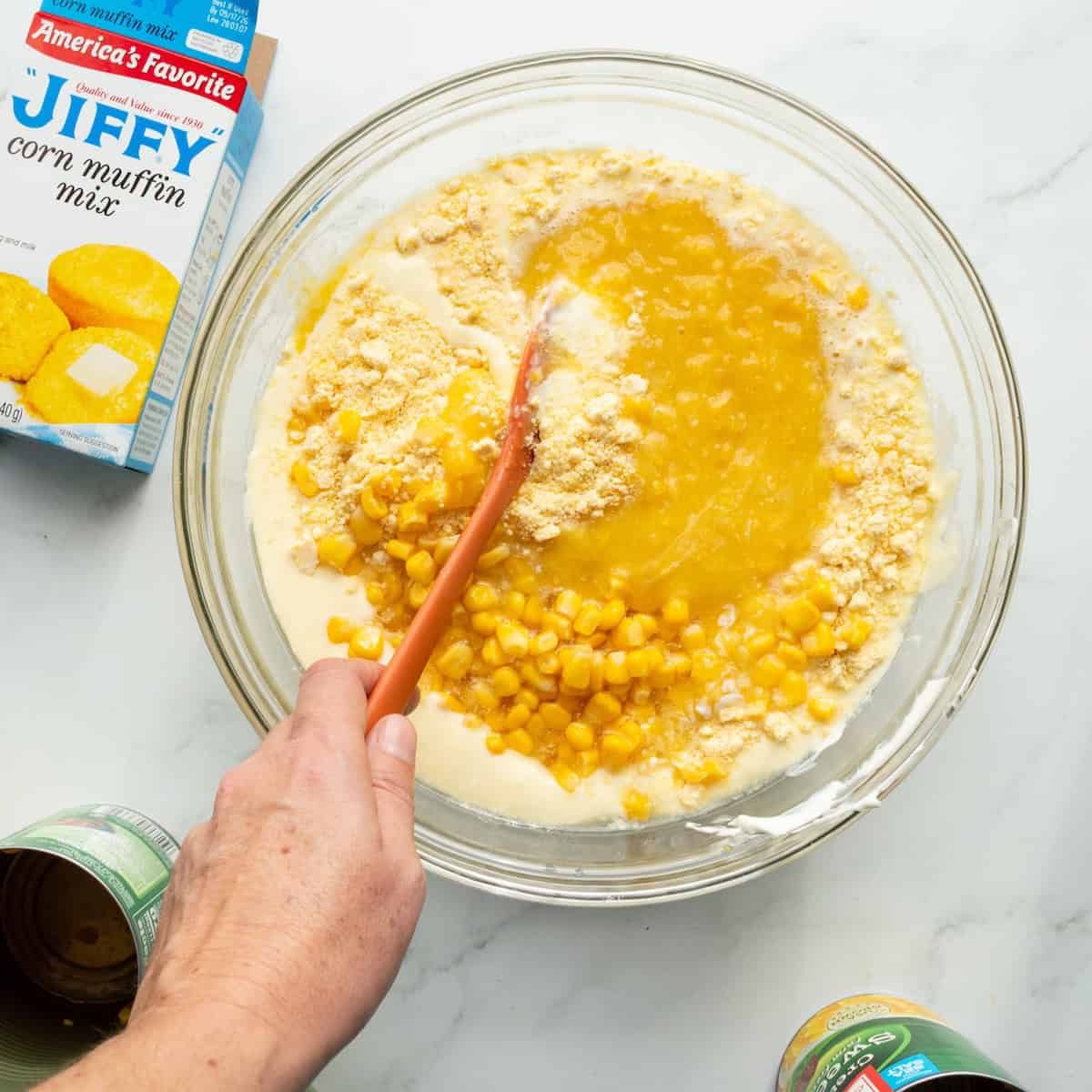 Combining the dry ingredients and wet ingredients of the Pollo Tropical corn souffle recipe in a glass bowl.