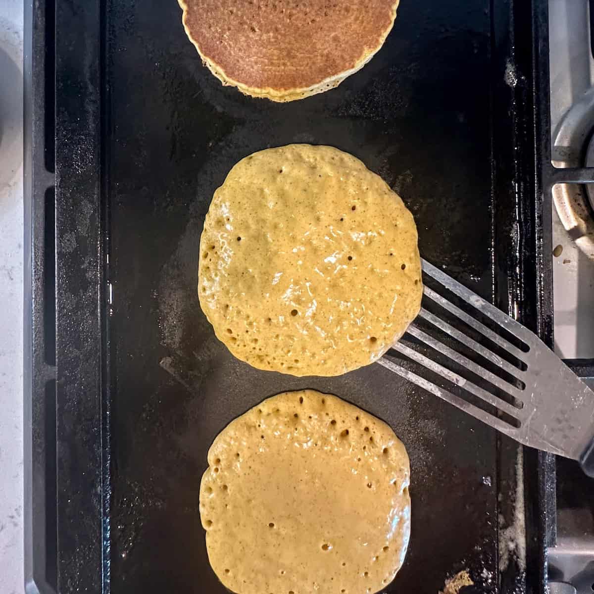 Flipping cooked pumpkin pancakes on a cast-iron griddle.