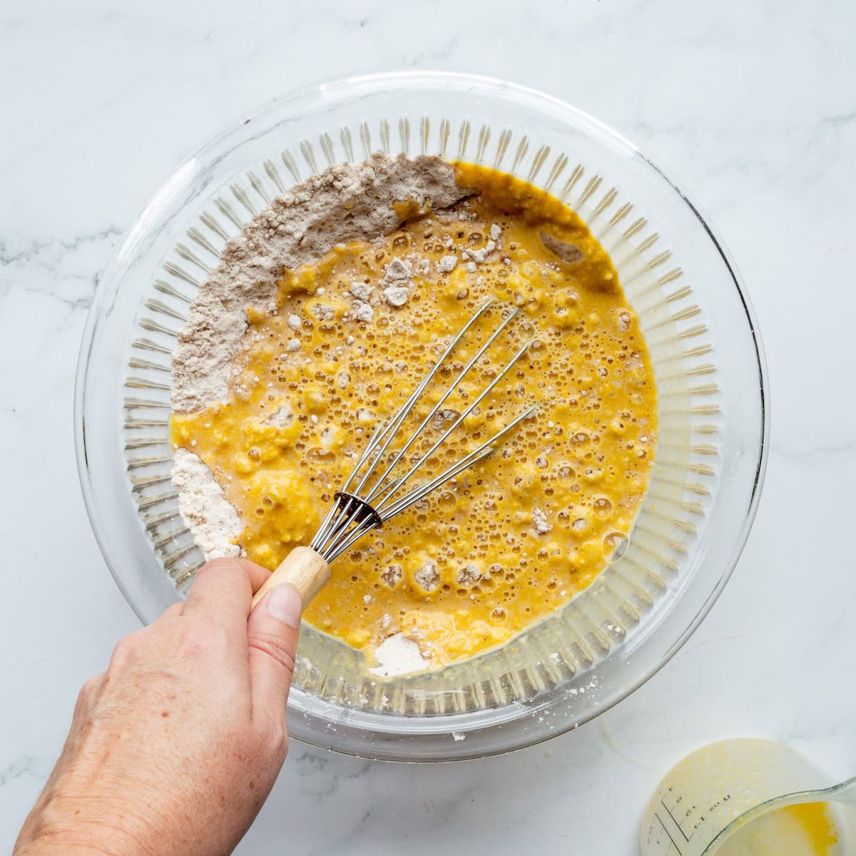 Whisking pumpkin pancake batter in a glass bowl.