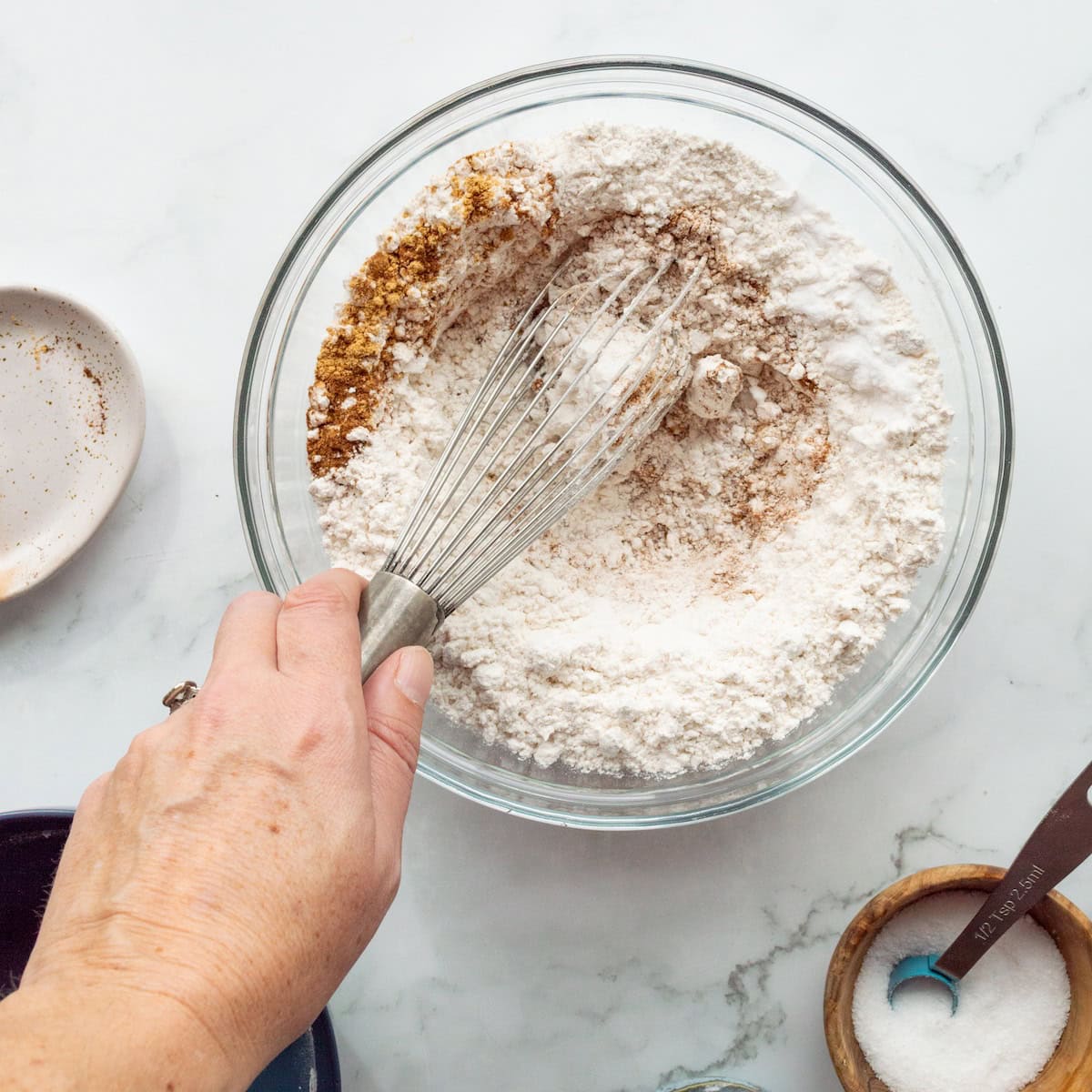 Whisking together the dry ingredients for ginger molasses cookies in a glass bowl.