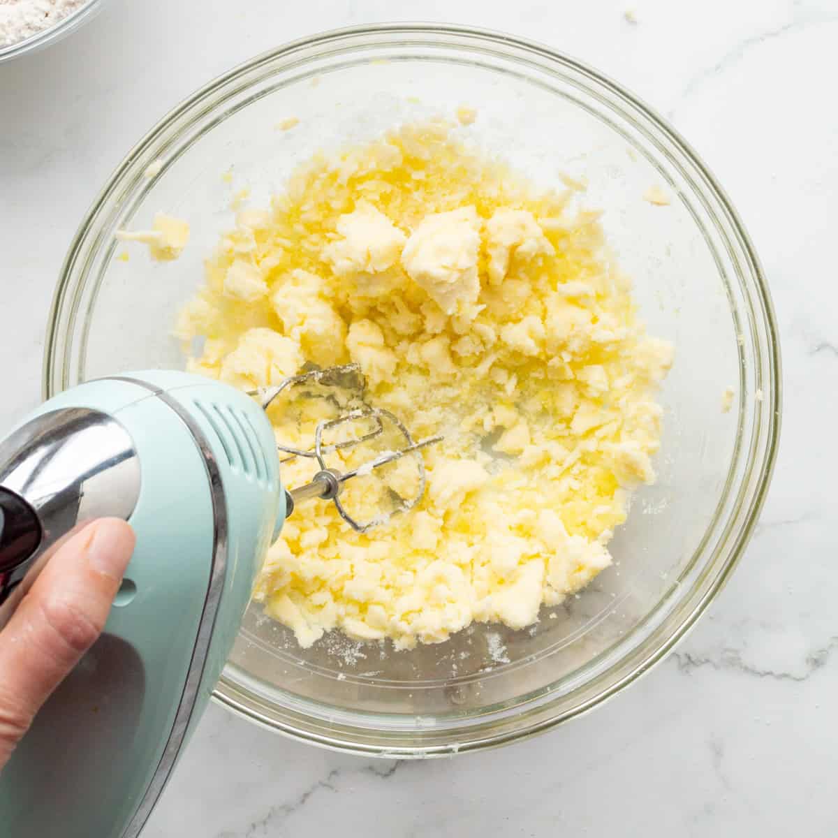 Creaming butter and sugar in a glass bowl with an aqua hand mixer.