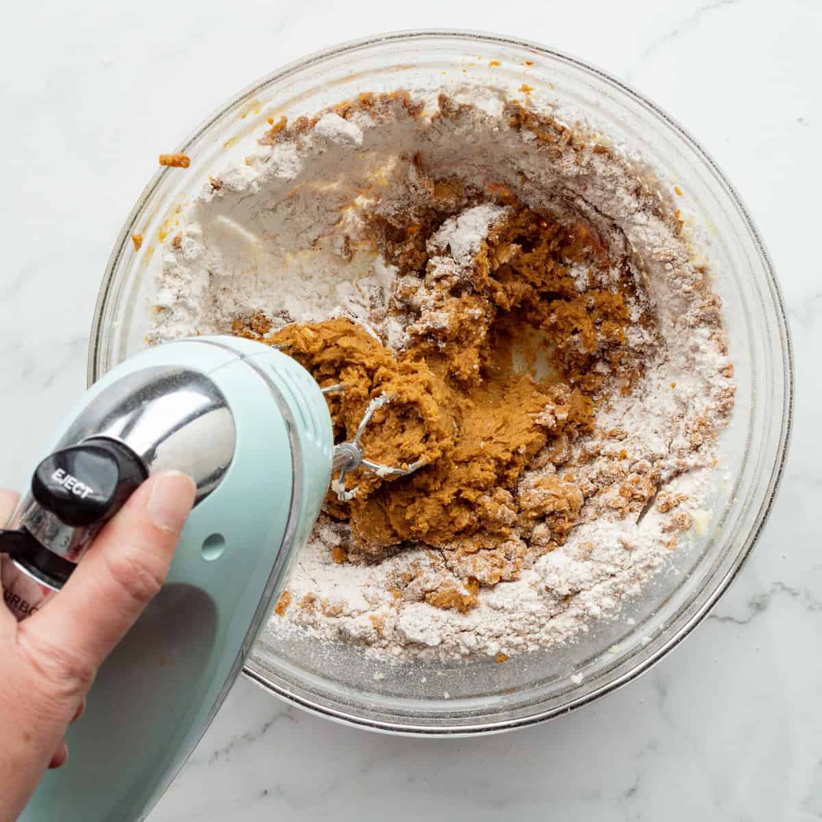 Blending the cookie dough for soft and chewy molasses cookies in a glass bowl with an aqua hand mixer.