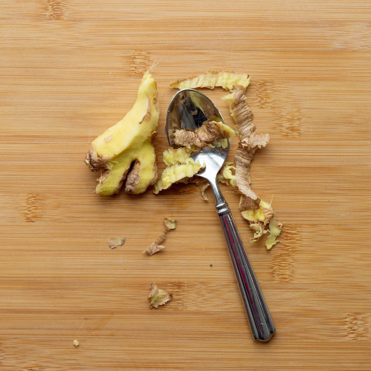 Peeling fresh ginger with a spoon on a wooden cutting board.