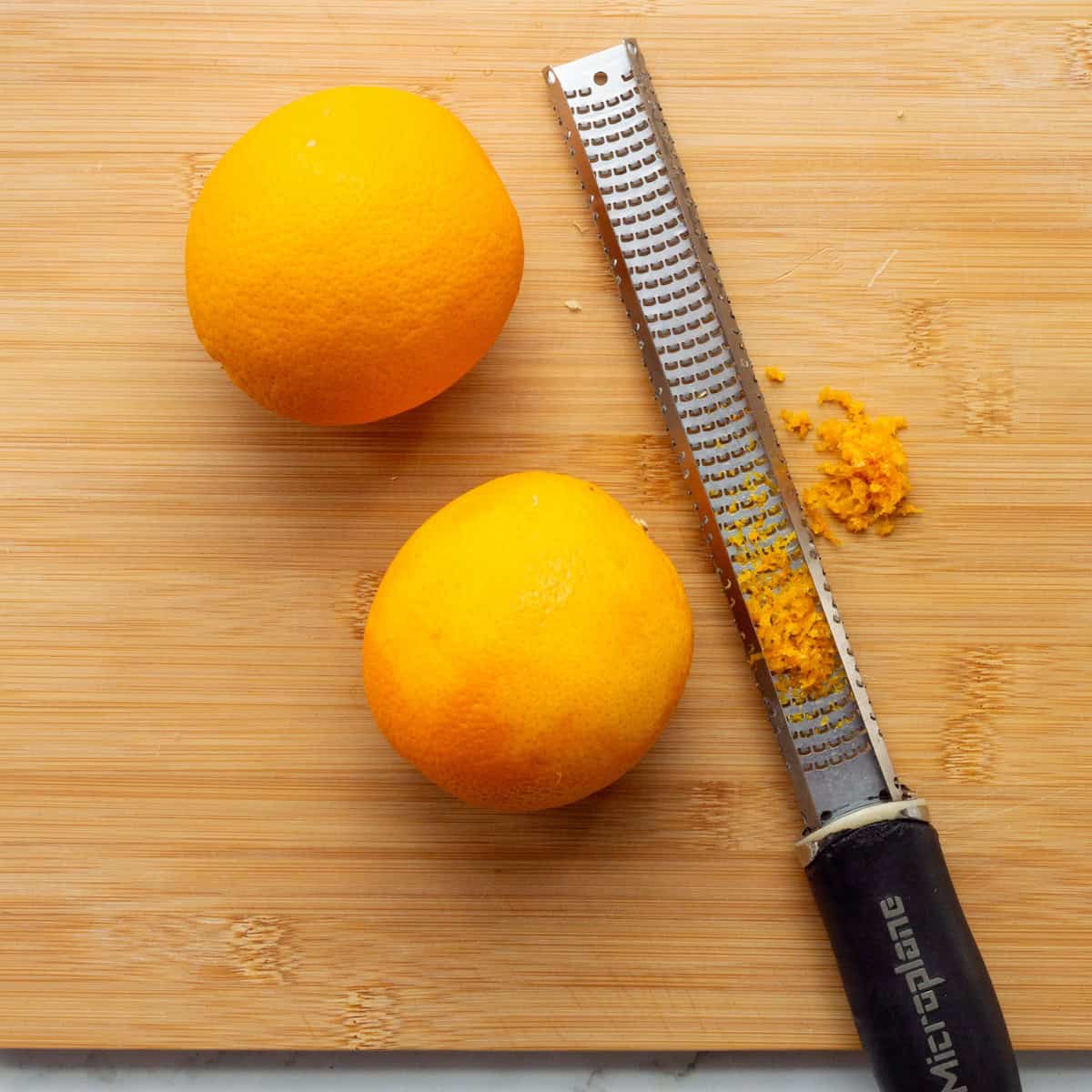 Grating orange zest on a wooden cutting board with a Microplane grater.