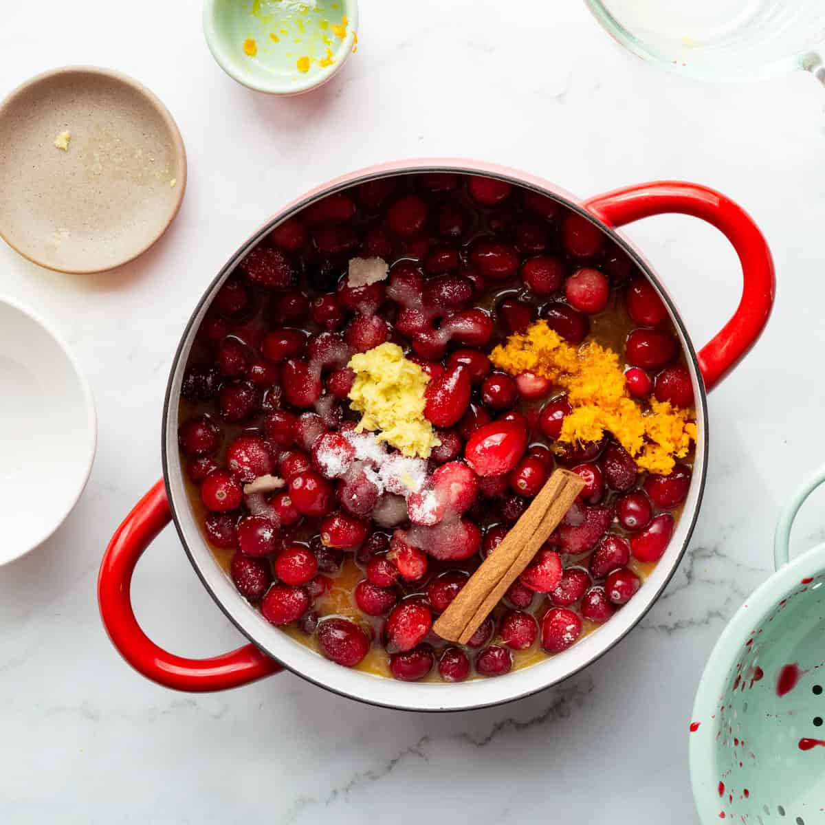 Combining the ingredients for homemade cranberry sauce in a red handled Dansk pot.