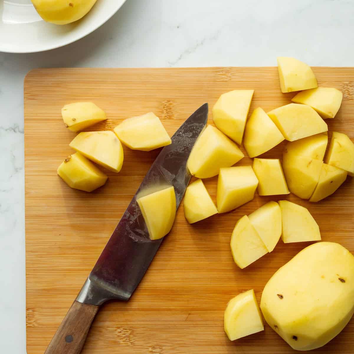 Cutting Yukon Gold potatoes into large chunks on a wooden cutting board.