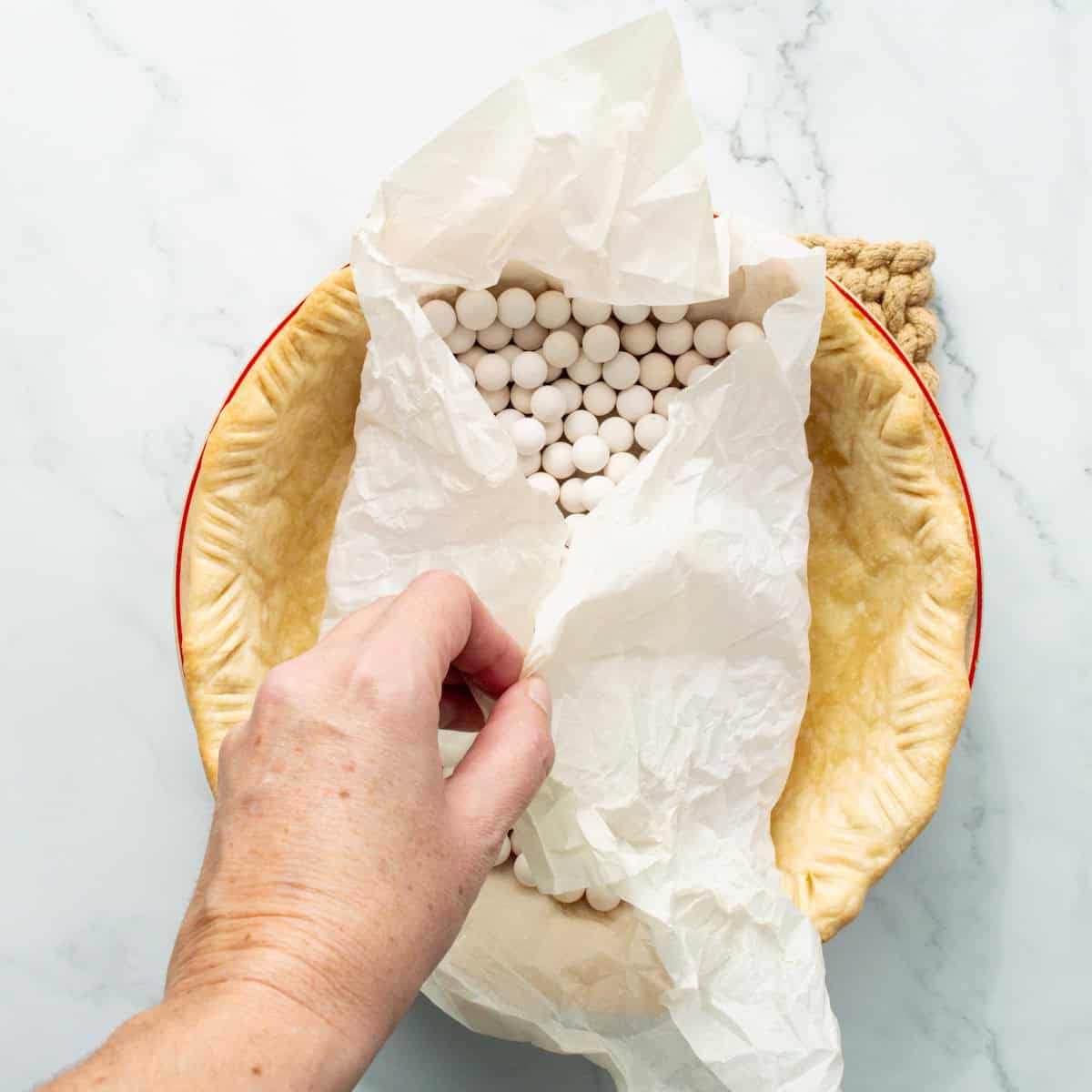 Removing parchment paper and ceramic pie weights from a par-baked pie crust.