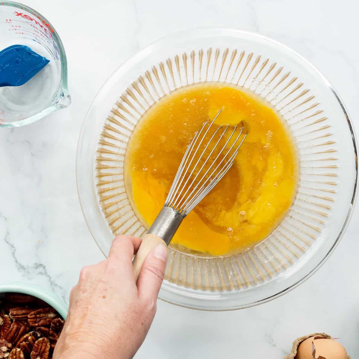 Whisking together the filling for Southern Bourbon Pecan pie in a glass bowl.