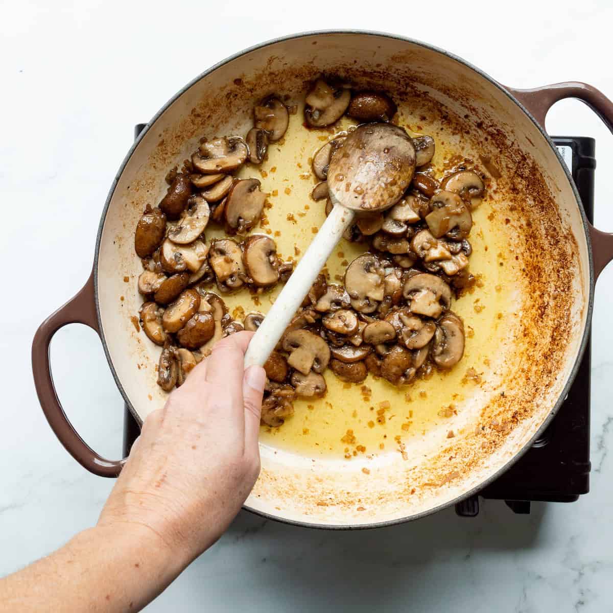 Sautéing mushrooms in a two-handled brown skillet.