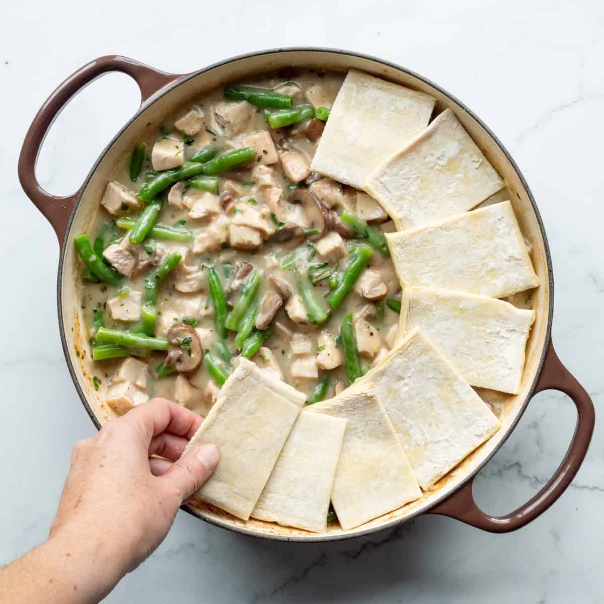 Place puff pastry squares on top of turkey pot pie filling in a dark brown handled cast-iron pan.