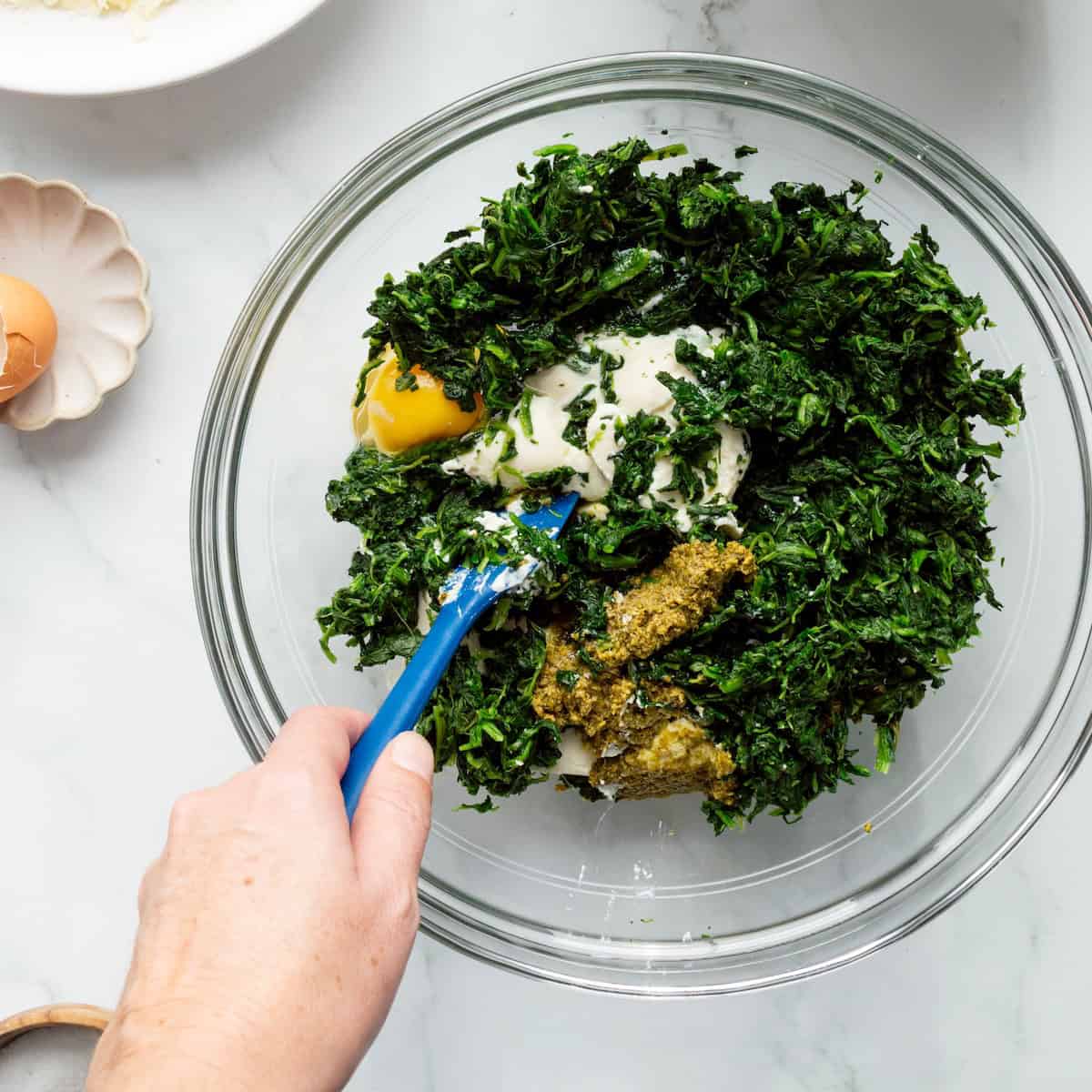Stirring together the ricotta and spinach filling for lazy ravioli lasagna in a glass bowl with a blue rubber spatula.