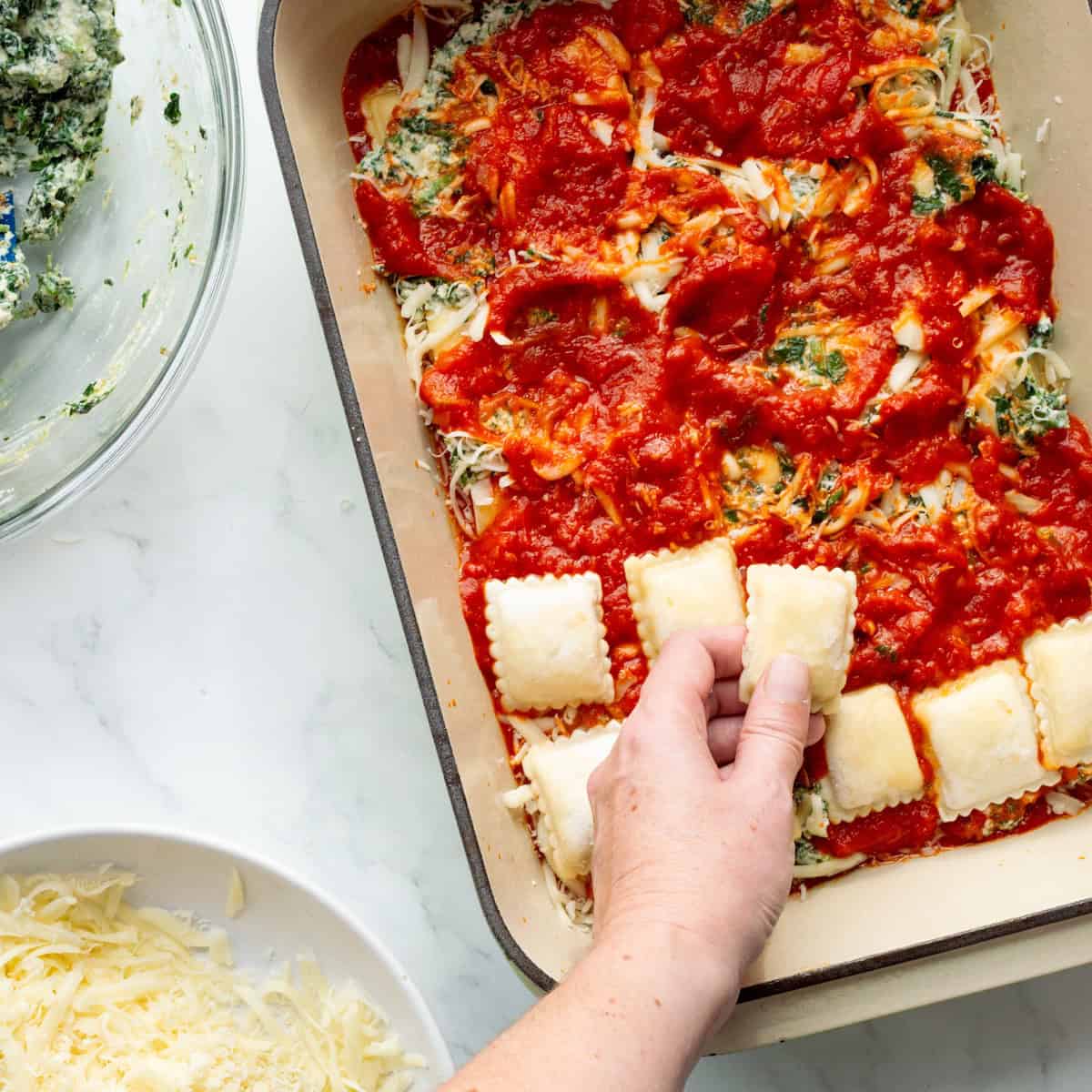 Layering frozen ravioli on top of marinara sauce in a casserole dish.