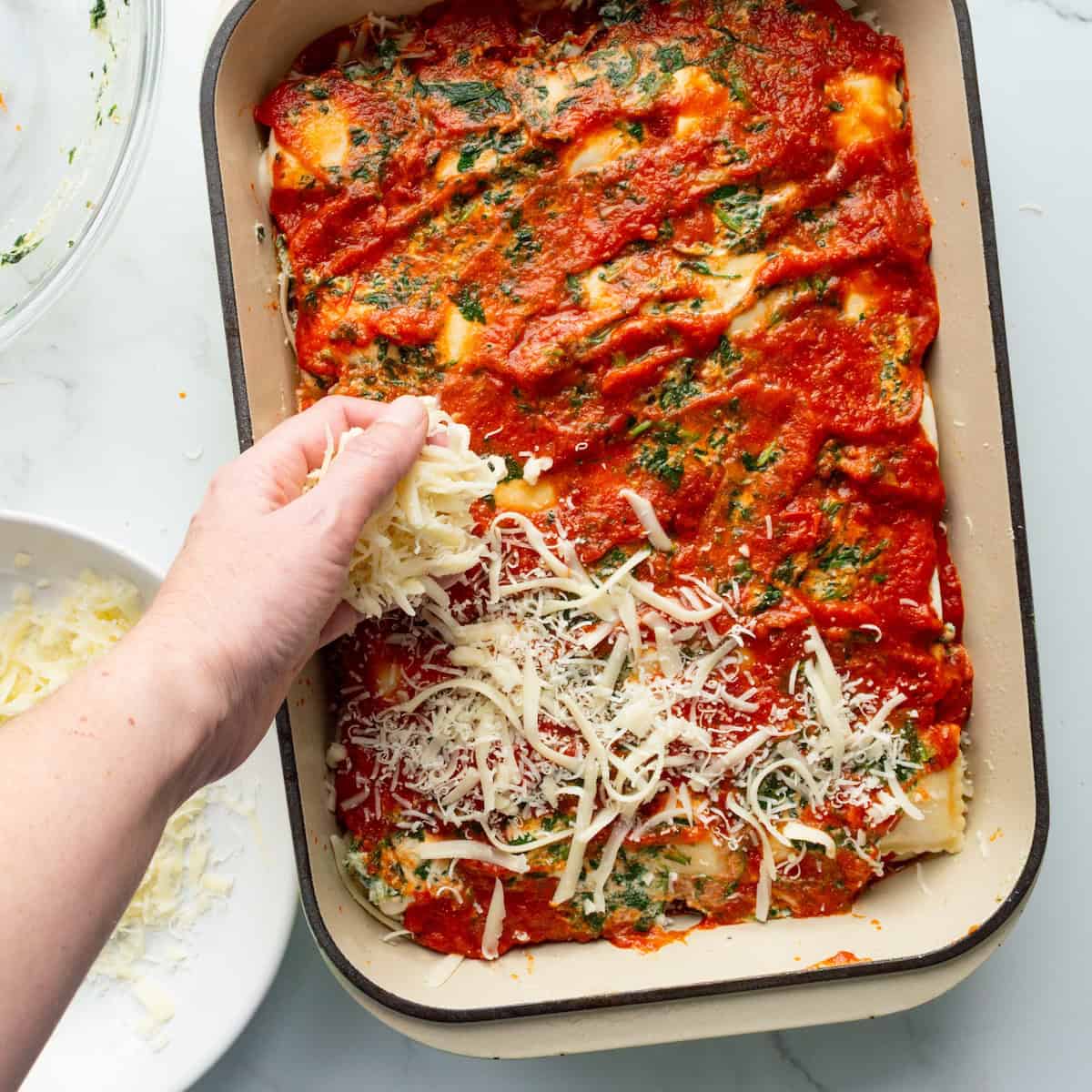 Sprinkling a white cheese blend on top of layered lasagna in a 13 x 9 inch baking dish.