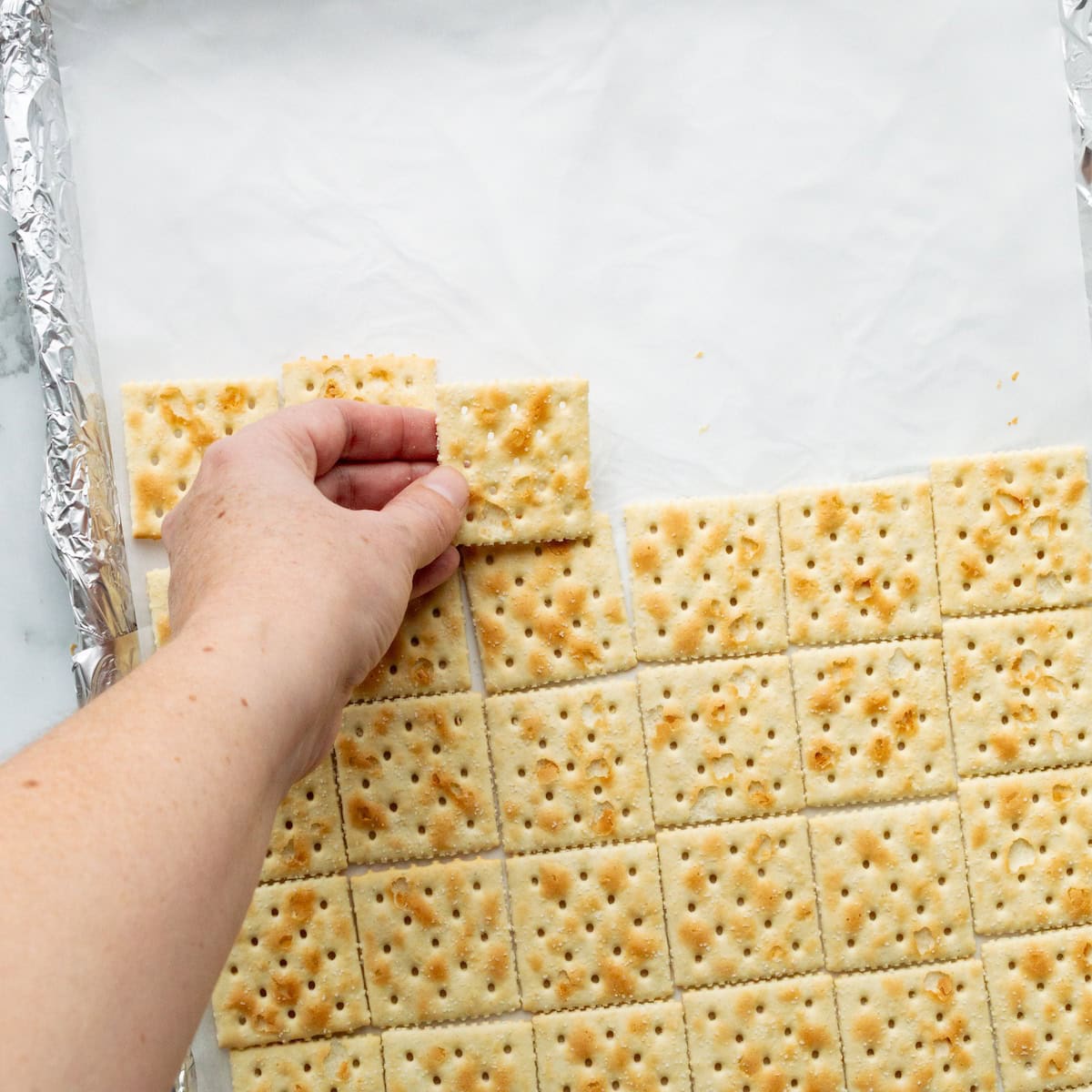 Arranging saltine crackers in a single layer on a parchment paper lined baking sheet.