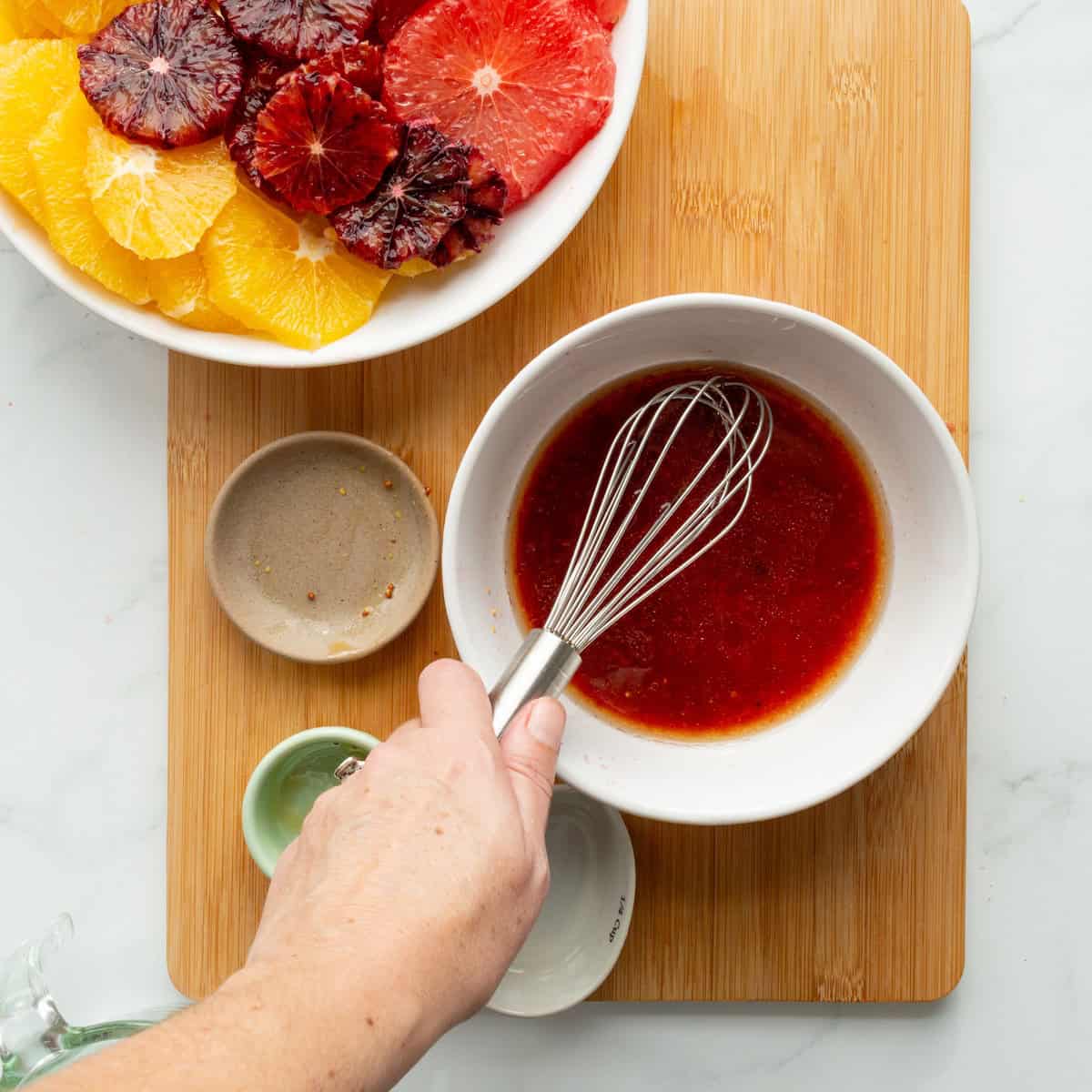 Whisking blood orange vinaigrette in a white bowl.