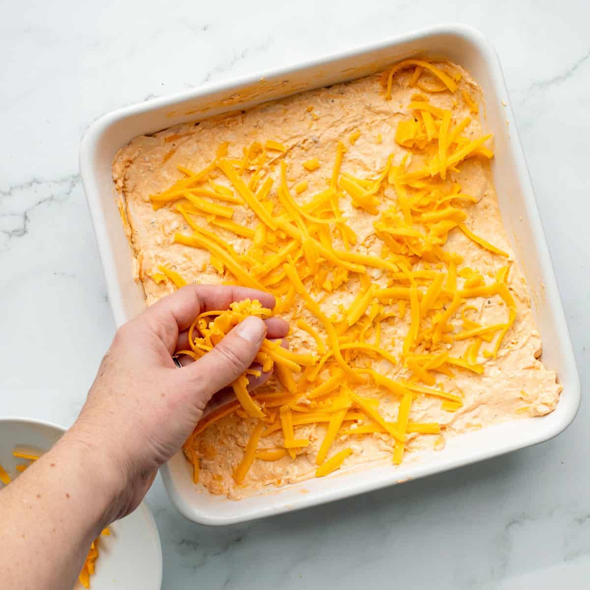 Sprinkling cheese onto the top of Frank's buffalo chicken dip.
