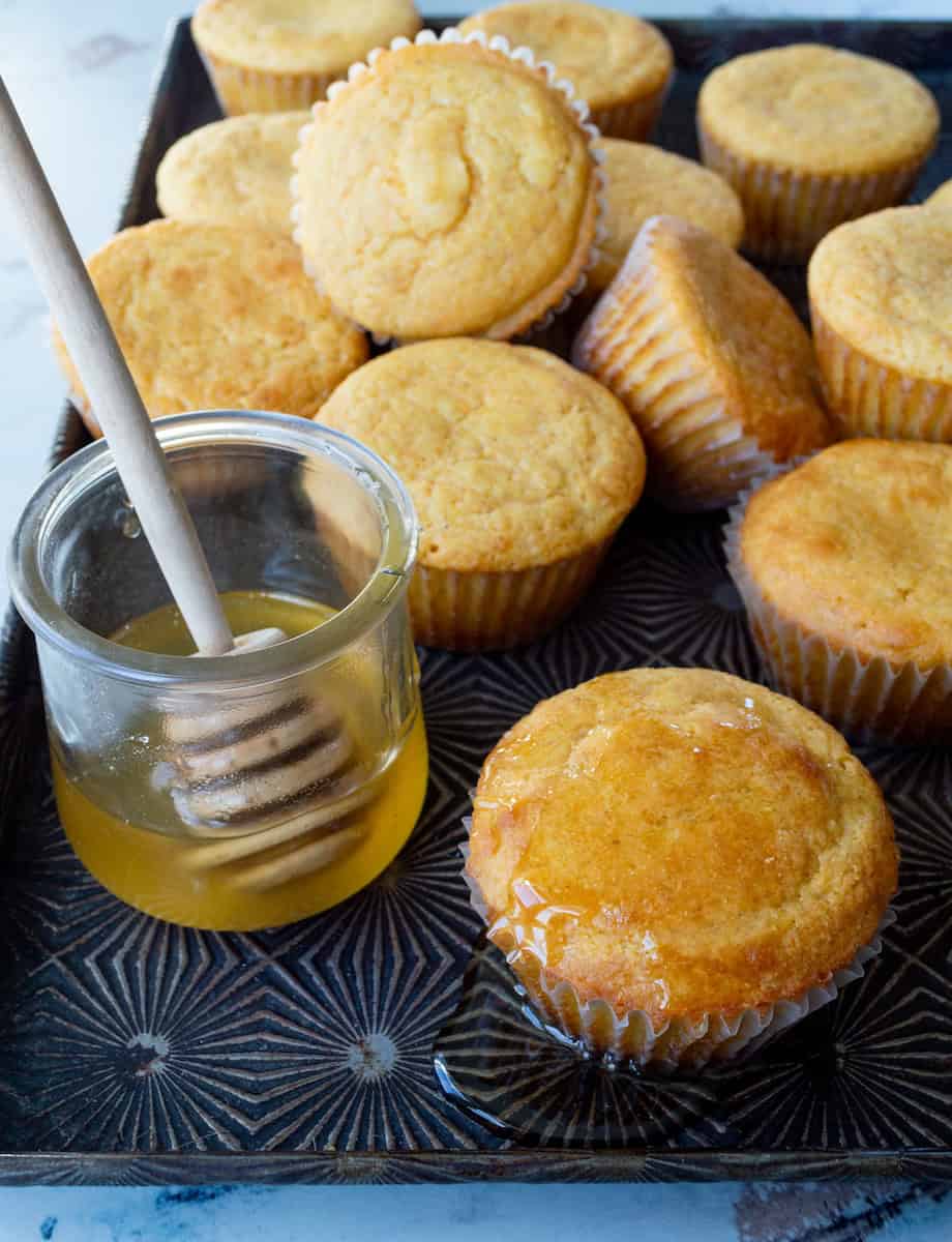 A metal Ovenex starburst pan of buttermilk cornbread muffins and a jar of honey with a honey wand.