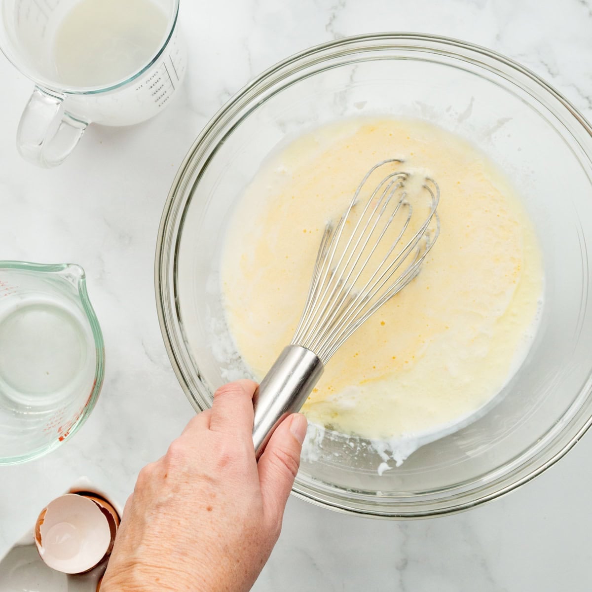 Whisking together buttermilk, oil, and eggs in a glass bowl for buttermilk cornbread.