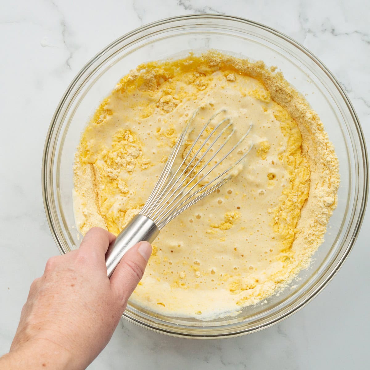 Whisking the buttermilk mixture into the cornmeal mixture for buttermilk cornbread in a glass bowl.