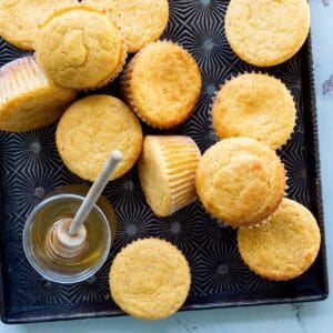 A metal Ovenex starburst pan of sweetie pie's buttermilk cornbread muffins and a jar of honey with a honey wand.