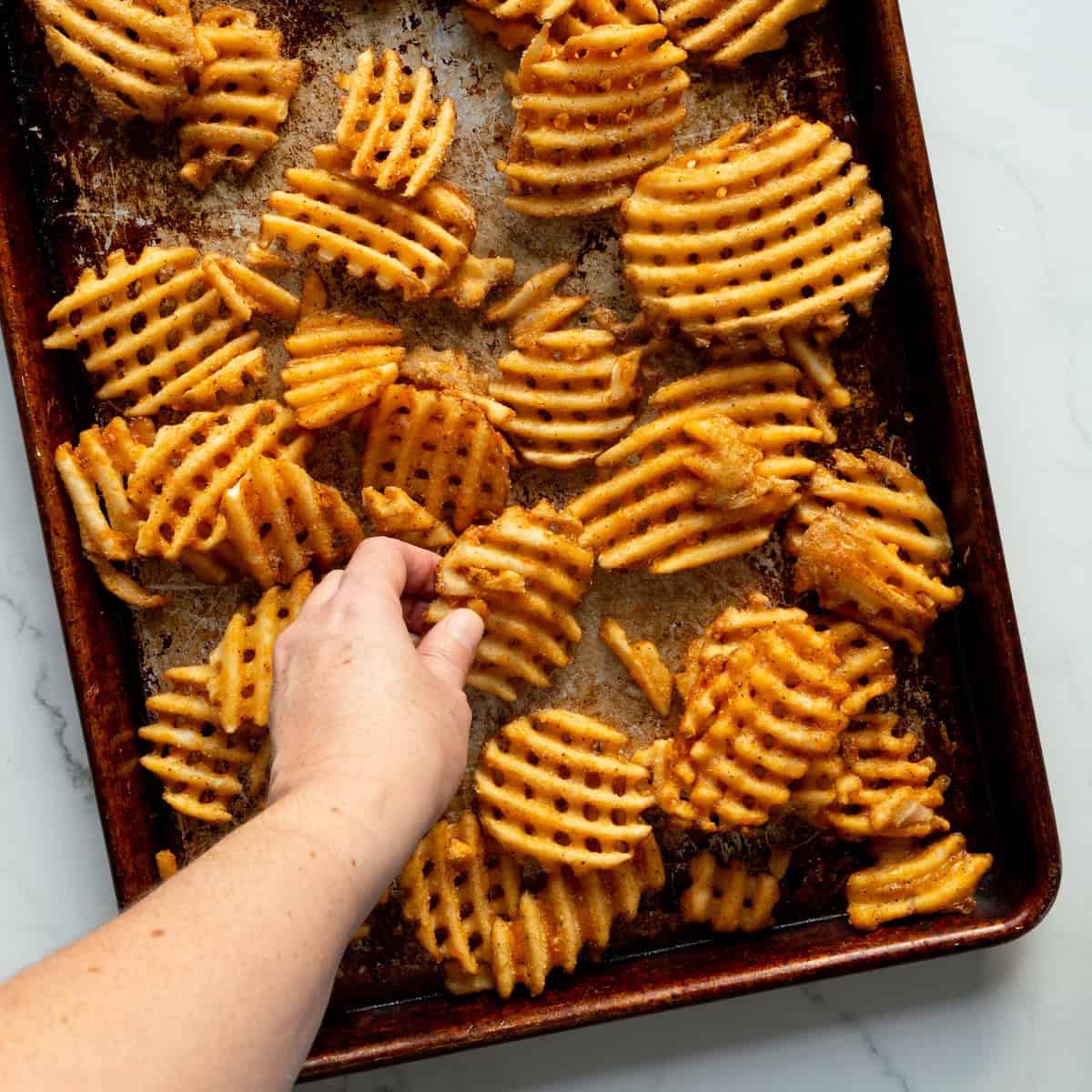 Arranging frozen waffle fries on a rimmed baking sheet in a single layer.